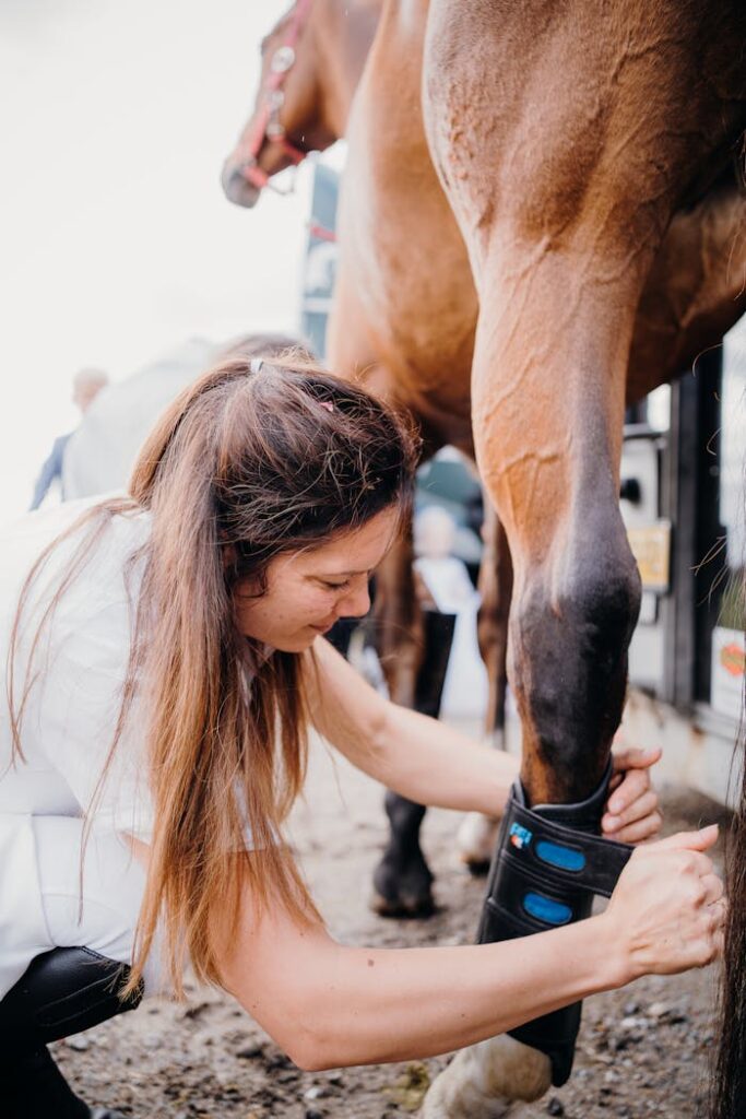 A woman carefully attends to a horse's leg, showcasing animal care and attention.